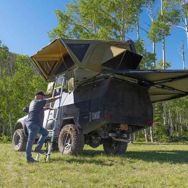 23zero-armadillo-a3-left-side-only-hard-shell-roof-top-tent-open-front-corner-view-on-vehicle-with-person-climbing-ladder-in-nature