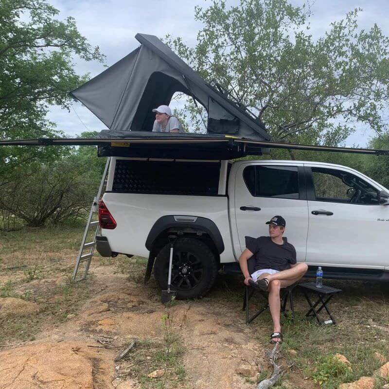 eezi-awn-blade-40th-edition-hard-shell-roof-top-tent-open-side-view-on-vehicle-with-persons-and-extended-awning-in-nature