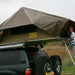 eezi-awn-jazz-soft-shell-roof-top-tent-open-rear-corner-view-on-vehicle-with-person-and-extended-ladder-in-nature