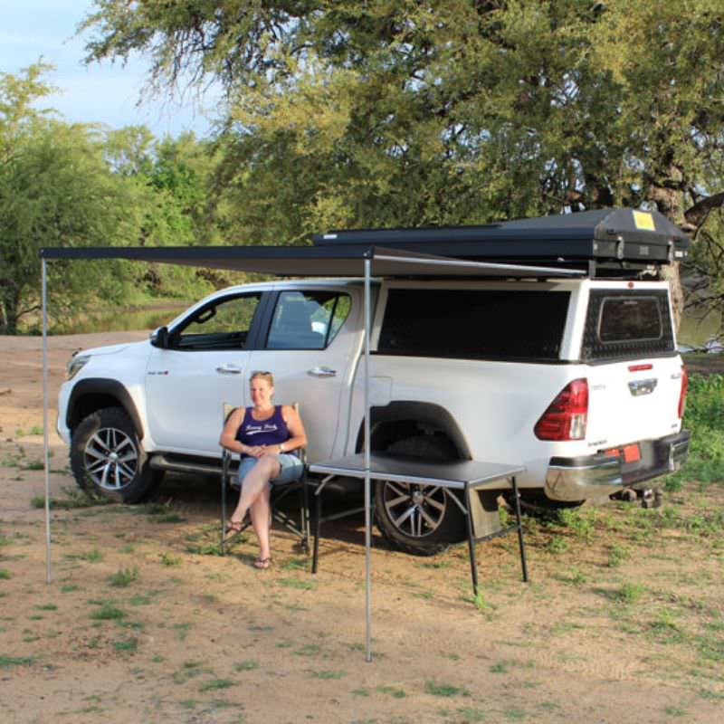 eezi-awn-series-1000-awning-gray-open-side-view-black-hardcase-with-person-on-toyota-tundra-in-terrain