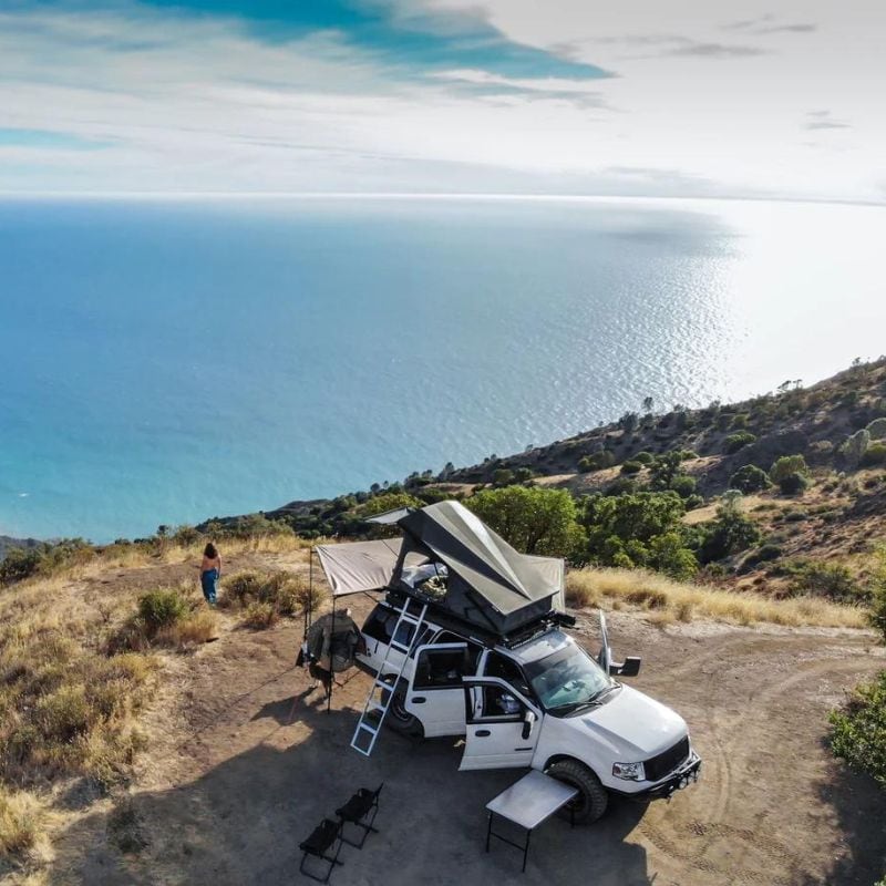 eezi-awn-stealth-hard-shell-roof-top-tent-open-drone-view-on-ford-explorer-with-person-outside-camping-at-view-point