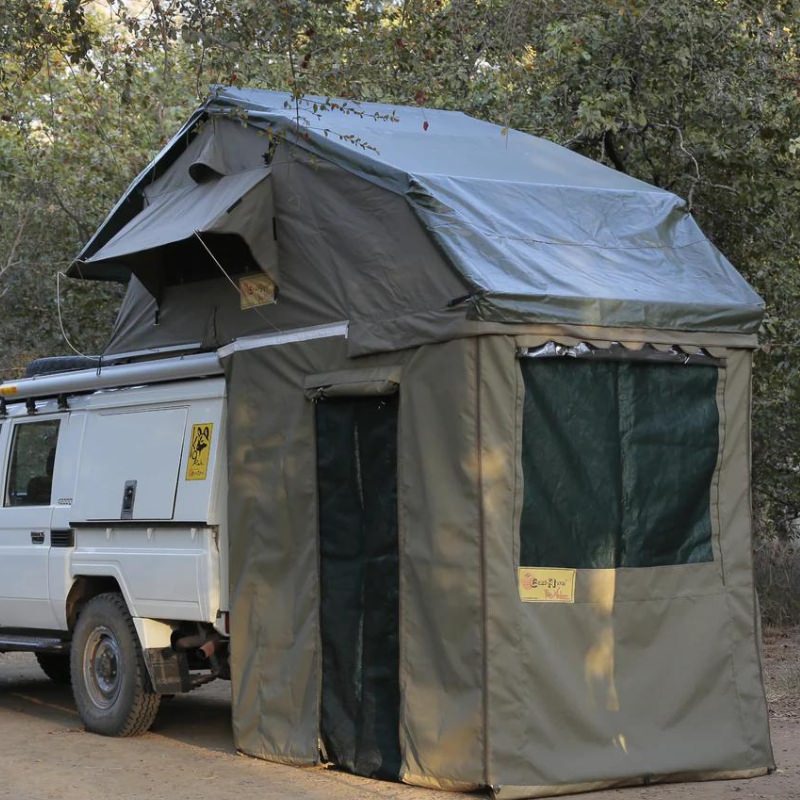 eezi-awn-xklusiv-soft-shell-roof-top-tent-olive-open-rear-corner-view-on-vehicle-with-extended-room-and-covered-door-in-nature
