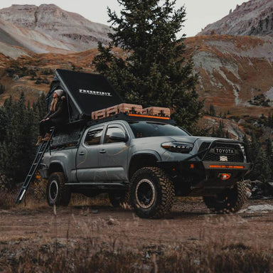 freespirit-recreation-aspen-v2-hard-shell-roof-top-tent-black-open-front-corner-view-on-toyota-tacoma-with-woman-in-nature