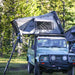 overland-vehicle-systems-bushveld-hard-shell-roof-top-tent-open-on-land-rover-defender-in-green-field