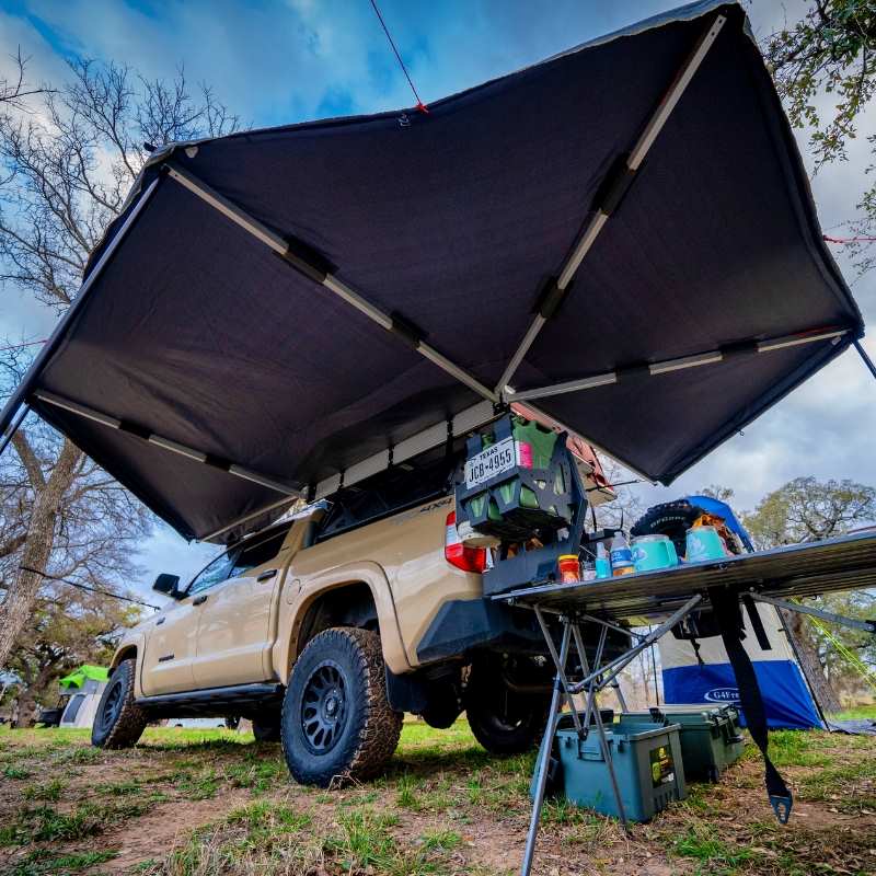 overland-vehicle-systems-nomadic-270-awning-driverside-open-rear-corner-view-on-toyota-tacoma-in-nature-camp