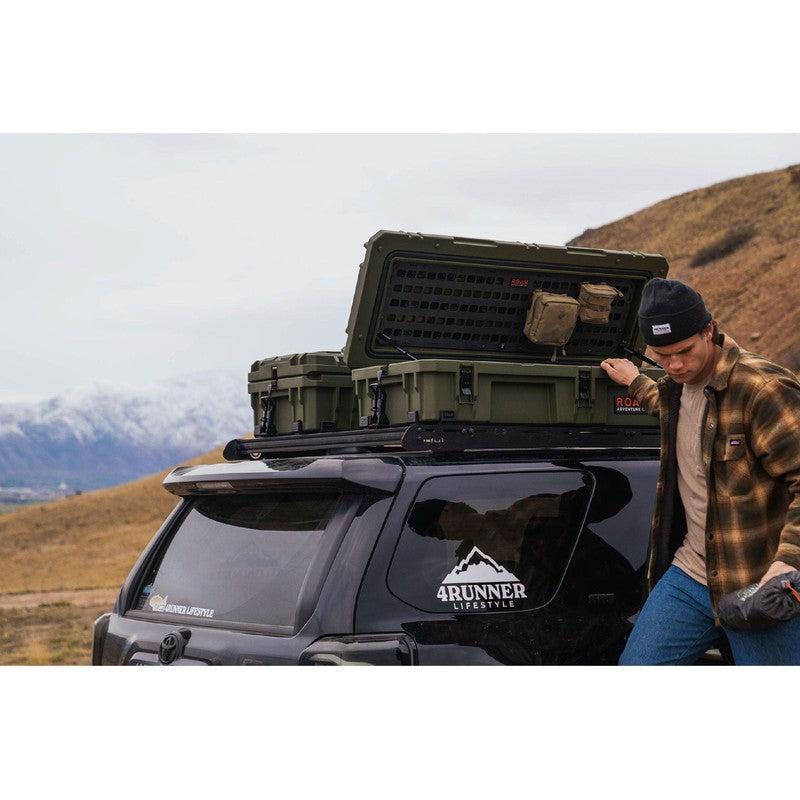 roam-95l-rugged-case-od-green-open-front-corner-view-on-vehicle-with-person-in-nature