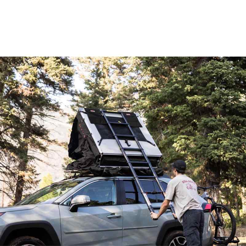 roam-vagabond-lite-rooftop-tent-black-closed-front-corner-view-on-toyota-rav4-with-person-holding-ladder-in-forest