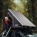 tentbox-cargo-hard-shell-roof-top-tent-black-open-rear-corner-view-on-vehicle-with-person-in-tent-in-nature
