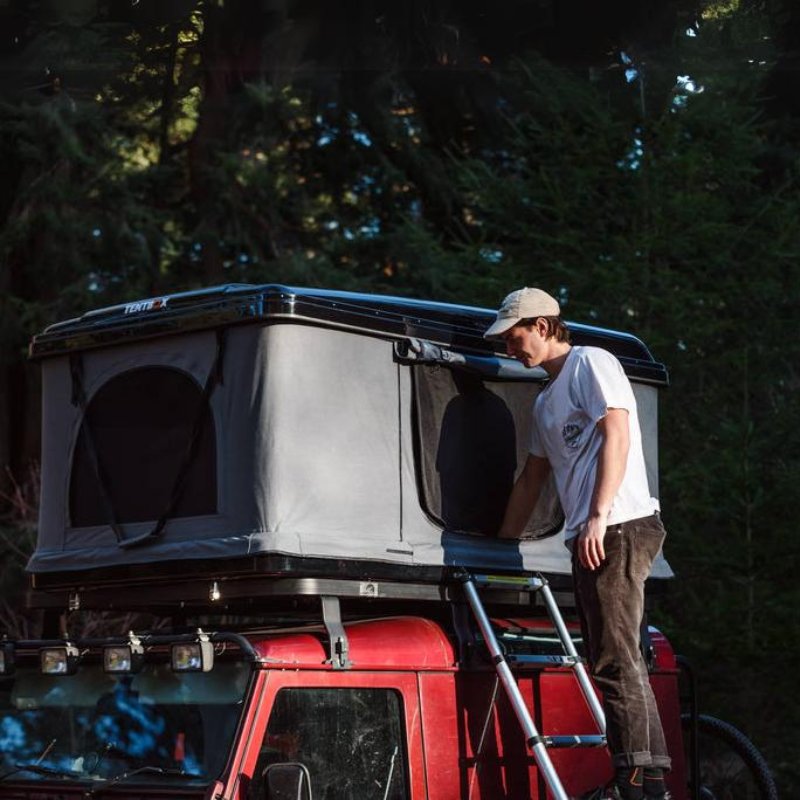  Analyzing image     tentbox-classic-hard-shell-roof-top-tent-gray-open-front-corner-view-on-vehicle-with-person-climbing-ladder-in-nature