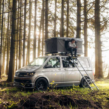 tentbox-classic-hard-shell-roof-top-tent-gray-open-front-corner-view-on-volkswagen-transporter-with-person-sitting-in-tent-in-nature